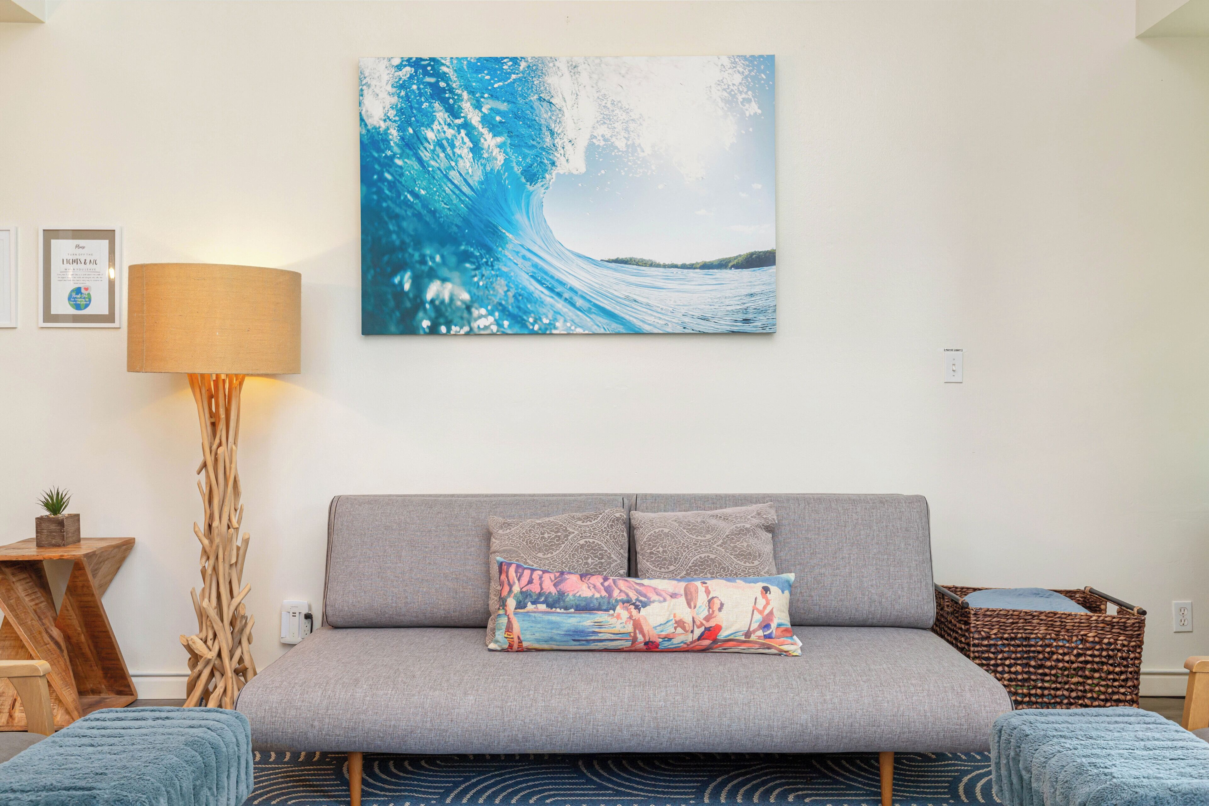 A living room with a grey sofa, a blue throw blanket, a wooden side table, a lamp, and a framed certificate on the wall.