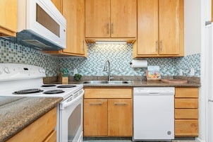 A kitchen with wooden cabinets, a white stove, a dishwasher, and a tiled backsplash.