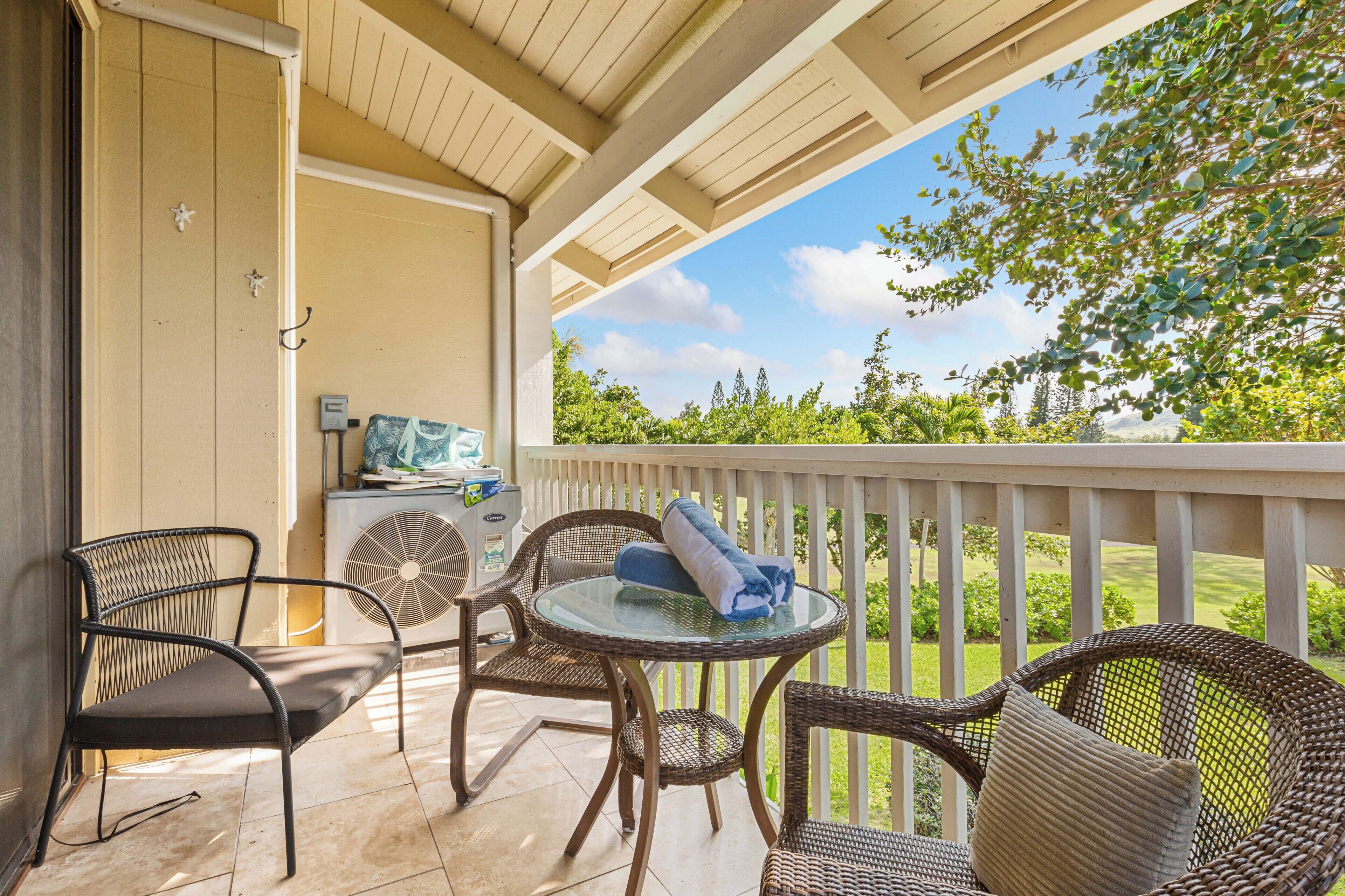 A covered outdoor seating area with wicker furniture and a glass table, overlooking a well-maintained garden.