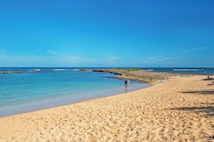 A sandy beach with clear blue water and a rocky outcrop.