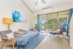 Quarto moderno com cama, sofá, poltrona e mesa. Há uma janela com cortinas e vista para árvores.