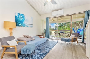 A modern room with a bed, a sofa, a chair, and a table. There is a window with curtains and a view of trees.
