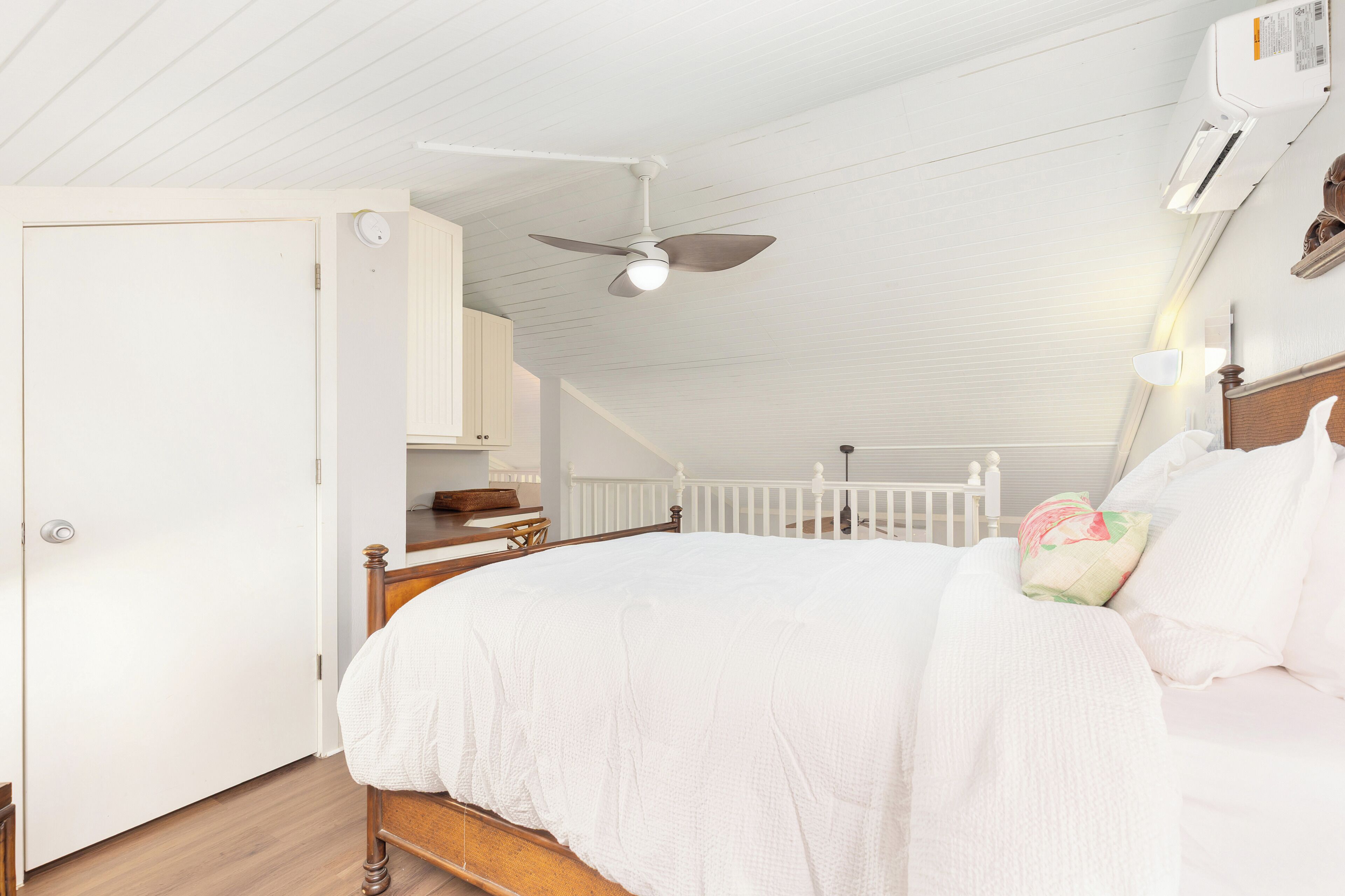 A bedroom with a wooden bed, white bedding, a ceiling fan, and an air conditioning unit.