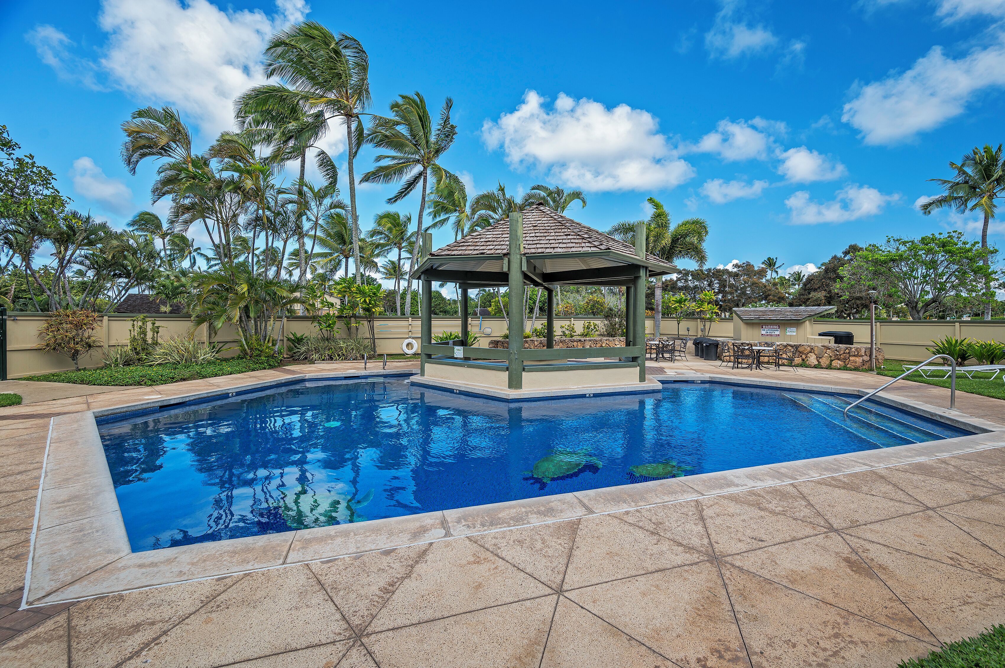 A swimming pool with a gazebo, palm trees, and a clear blue sky.