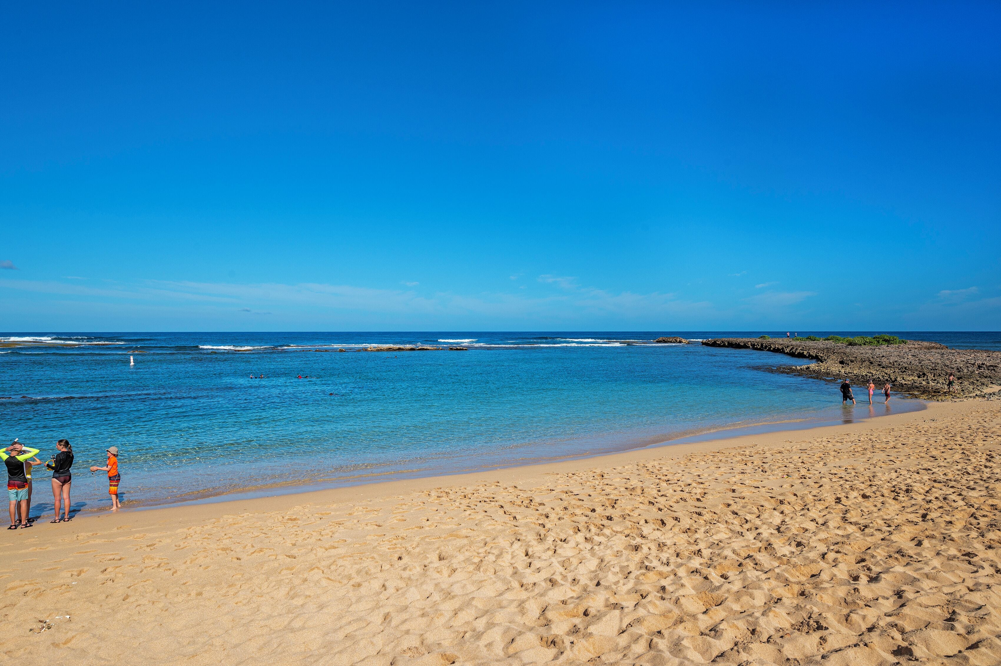 Una playa arenosa con agua azul cristalina y un litoral rocoso.