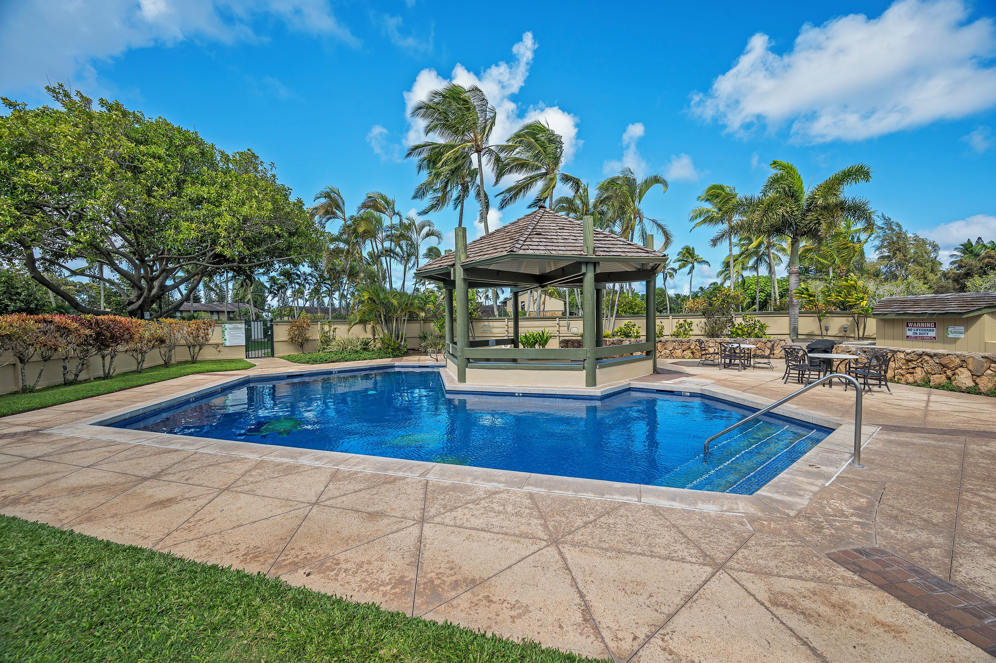 A swimming pool with a gazebo, palm trees, and a stone patio.