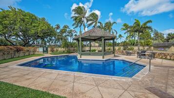 A swimming pool with a gazebo, palm trees, and a stone patio.