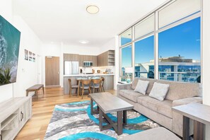 A modern living room with a sofa, coffee table, and a view of the city through large windows. - Breathtaking Ocean View Penthouse in the Heart of Honolulu (Honolulu)