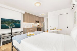 A modern hotel room with a bed, a desk, a kitchenette, and a TV displaying a scenic view. - Chic Studio With Skyline Views at The Park on Keeaumoku (Honolulu)