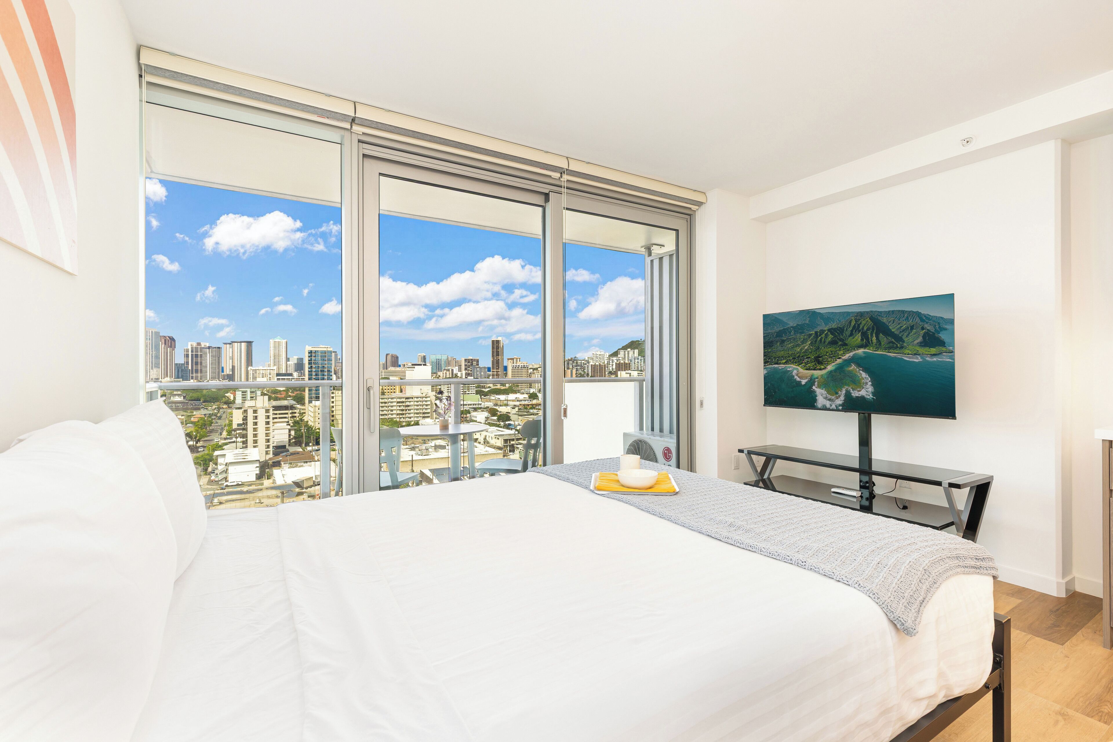 Ein Hotelzimmer mit einem großen Bett, einem Fernseher und Blick auf die Stadt durch raumhohe Fenster.