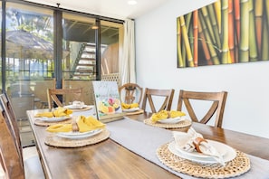 Uma área de refeições com mesa de madeira posta para quatro pessoas, porta de vidro que dá para o exterior e um quadro na parede.