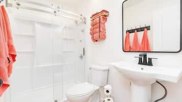 Ein Badezimmer mit Duschkabine aus Glas, einer weißen Toilette, einem Waschbecken mit Spiegel und Handtüchern an einem Wäscheständer.