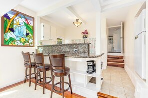 A kitchen with a granite countertop, a coffee maker, and a bar stool area.