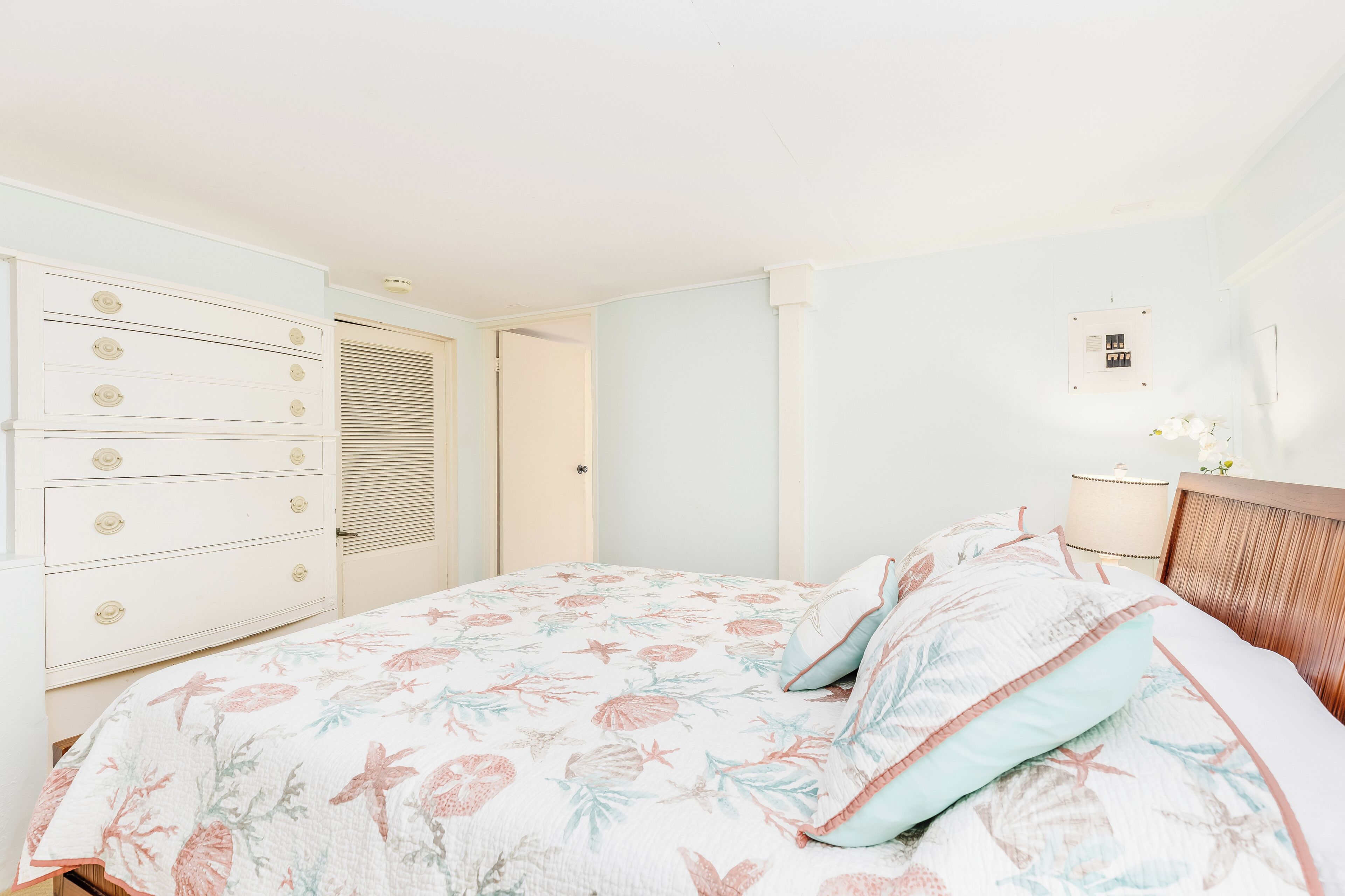 Een slaapkamer met een bloemenbedekker, een houten hoofdbord en een witte dressoir met laden.