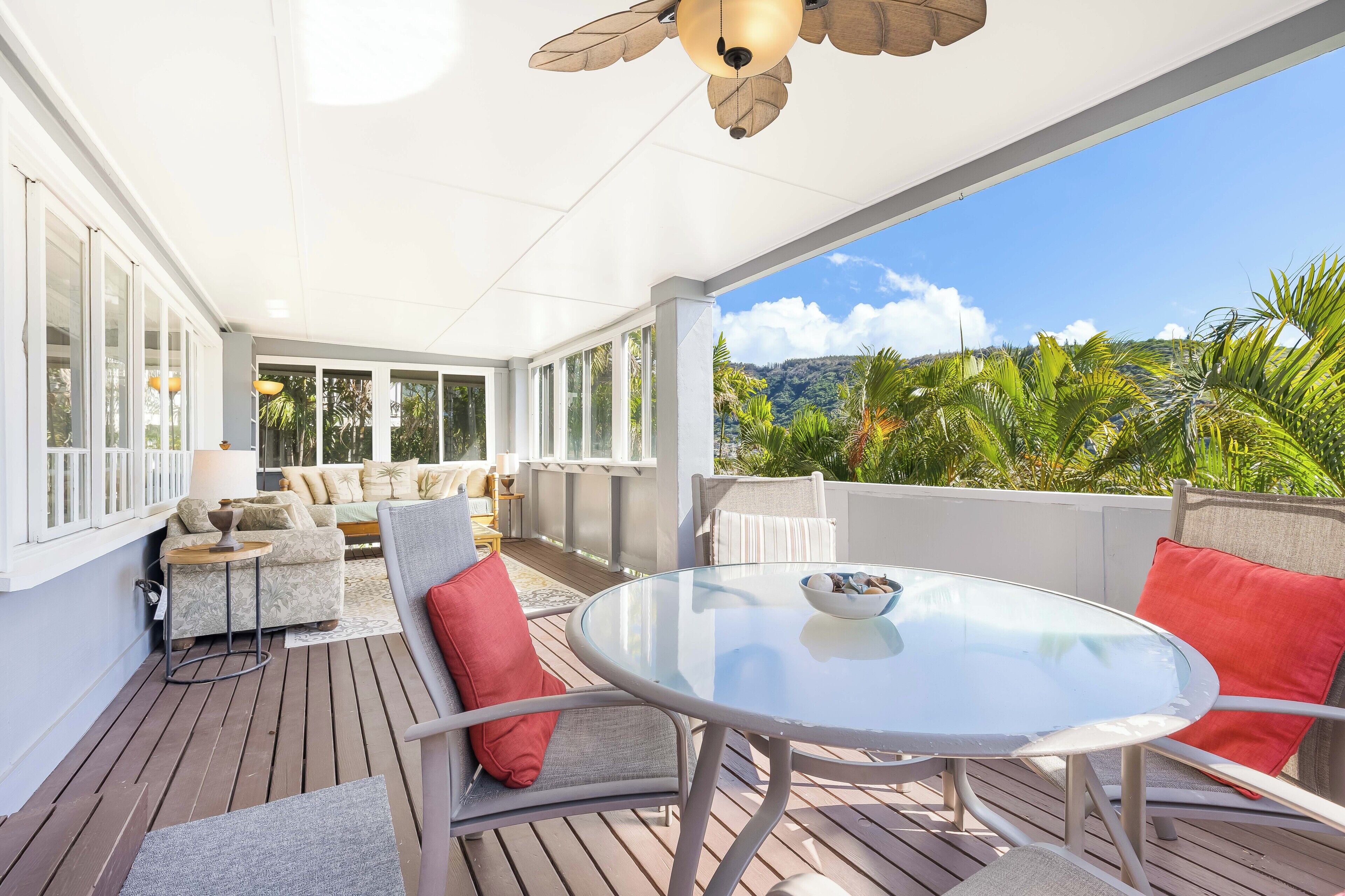 Un espace extérieur abrité avec une table et des chaises en verre, un canapé et un ventilateur de plafond.