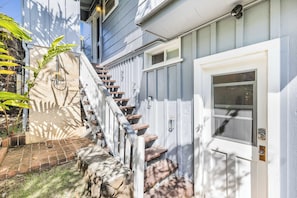 A staircase leading to a white door with a window, surrounded by greenery and a stone wall.