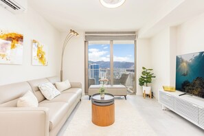 Ein modernes Wohnzimmer mit einer Couch, einem Couchtisch, einem Fernseher und einem großen Fenster mit Blick auf die Stadt.