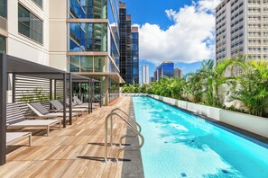 A rooftop pool with sun loungers and a view of tall buildings. - Sky Ala Moana Luxury Getaway With Ocean-city Views & Amazing Resort Amenities (Honolulu)