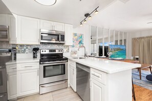 A modern kitchen with white cabinetry, stainless steel appliances, and a large island with a sink. - Skyline-lagoon and Fireworks Magic From the Ilikai W/top-tier Amenities (Honolulu)
