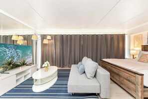 Een moderne hotelkamer met een groot flatscreen televisietoestel, een bank, een houten bedframe en een blauw gestreept vloerkleed.