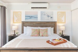 A neatly made bed with a wooden headboard, two bedside tables with lamps, and a tray with a pastry on the bed. - Stunning Ocean & Fireworks Lagoon View From Condo at Ilikai W/full Kitchen (Honolulu)