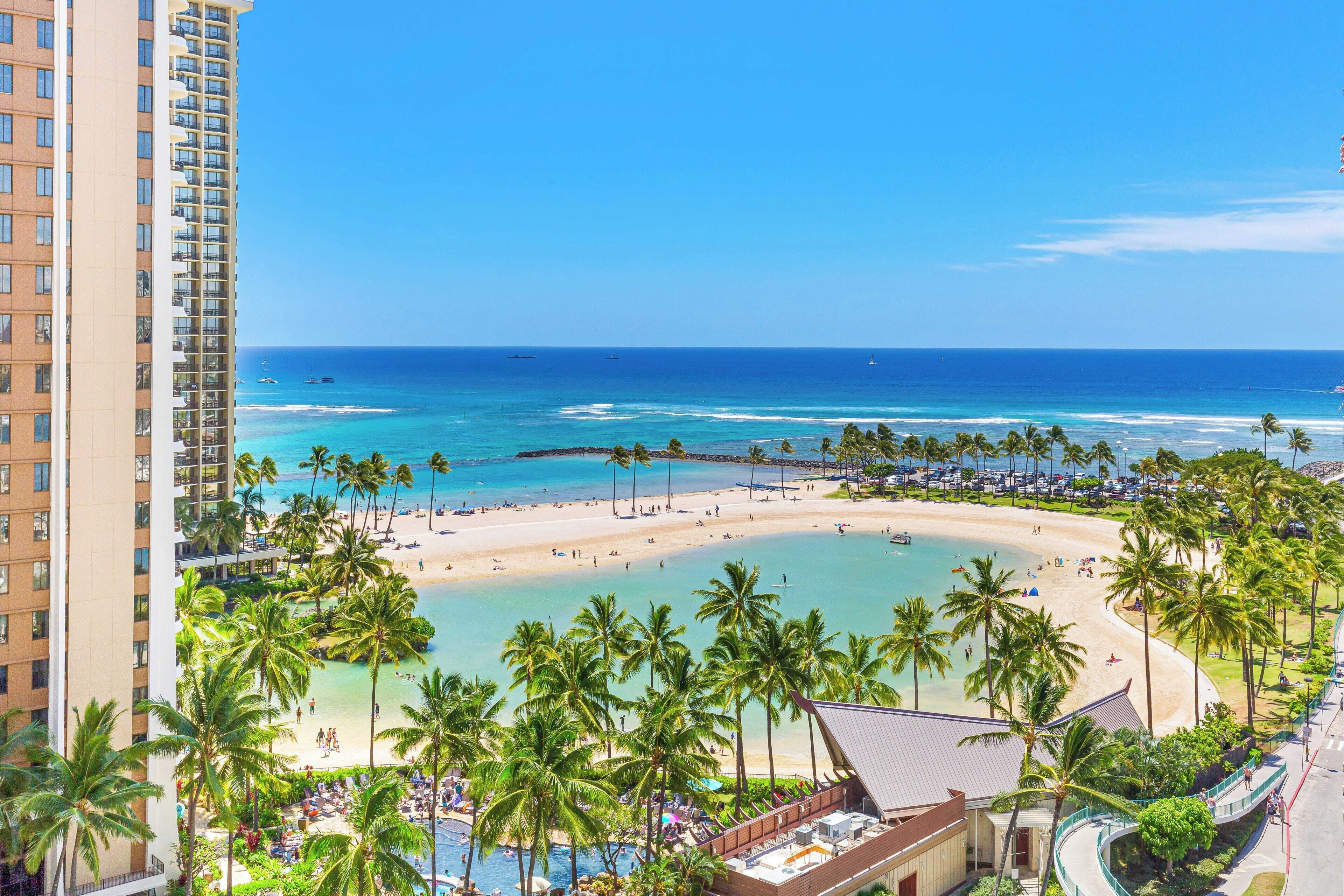 A beachfront hotel with a pool, beach, and palm trees.