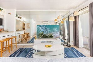 A modern kitchen with a large island, wooden stools, and a large TV screen. - Stunning Ocean & Fireworks Lagoon View From Condo at Ilikai W/full Kitchen (Honolulu)