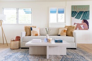 A living room with a sofa, a coffee table, a rug, and a wall with a painting. - Serene Lanikai House Near the Beach W/outdoor BBQ & Close to Shopping Center (Kailua)