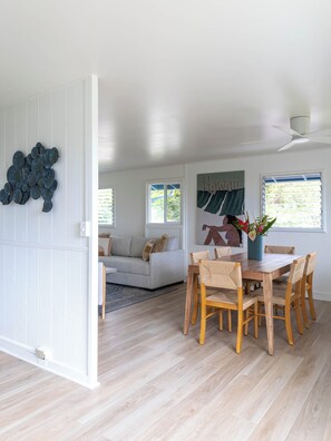 A spacious living area with a dining table and chairs, a sofa, and a decorative wall piece. - Serene Lanikai House Near the Beach W/outdoor BBQ & Close to Shopping Center (Kailua)