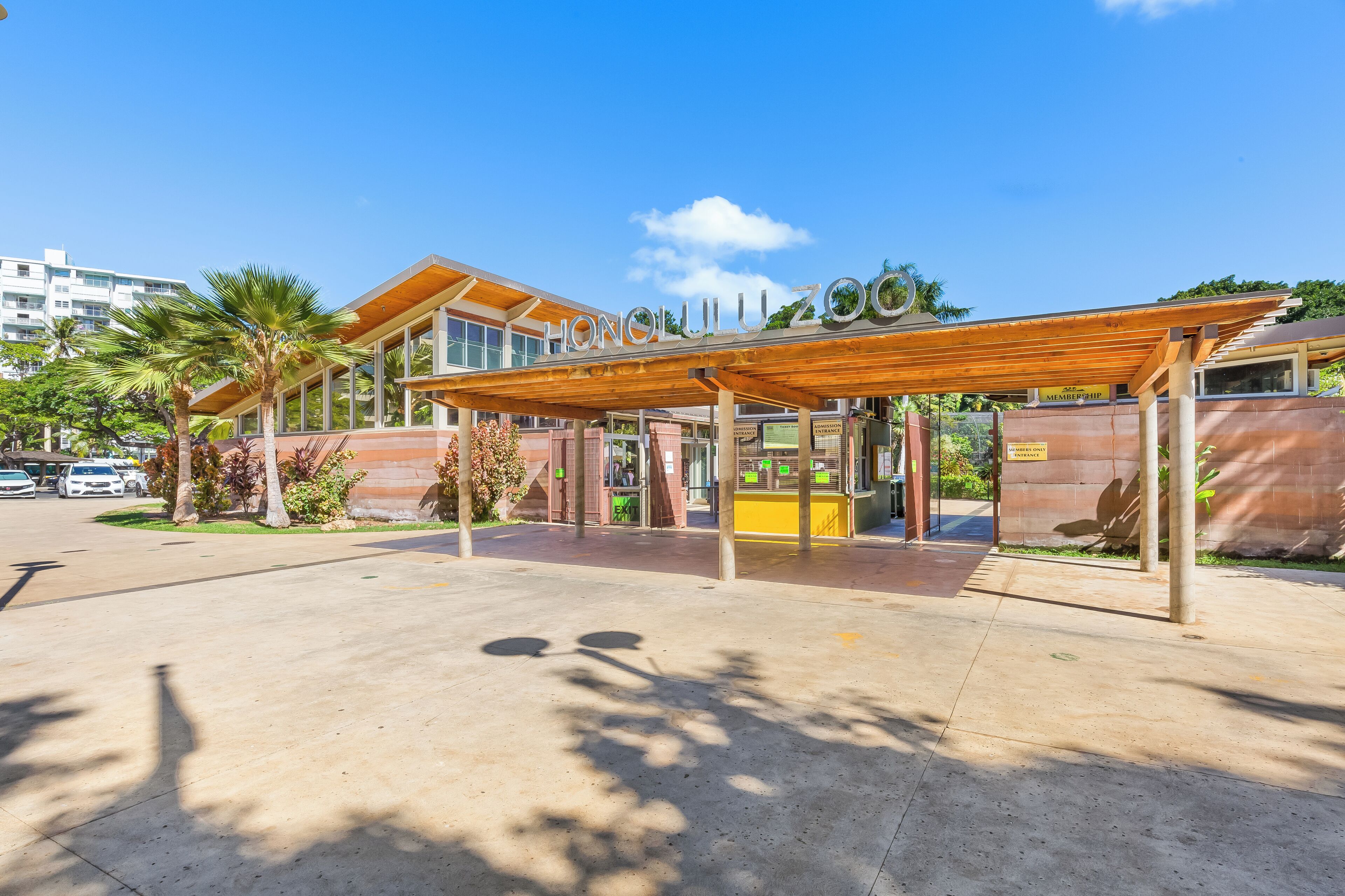 A zoo entrance with a covered walkway, palm trees, and a clear blue sky.