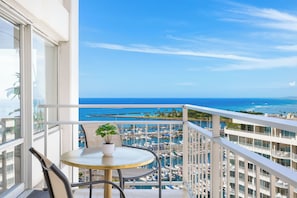 A balcony with a table and chairs, overlooking a marina with boats and a clear blue sky. - Ocean-sunset Views Condo Steps Away From the Beach W/awesome Ilikai Amenities (Honolulu)