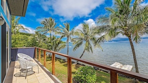 Un balcone con vista sul mare, palme e una ringhiera in legno.