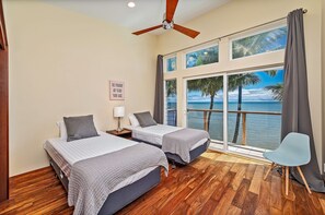 A bedroom with two beds, a ceiling fan, a window with a view of the sea, and a chair. - Oceanfront Gem in the Beautiful Kaneohe Dream Home Paradise Family Retreat (Kaneohe)