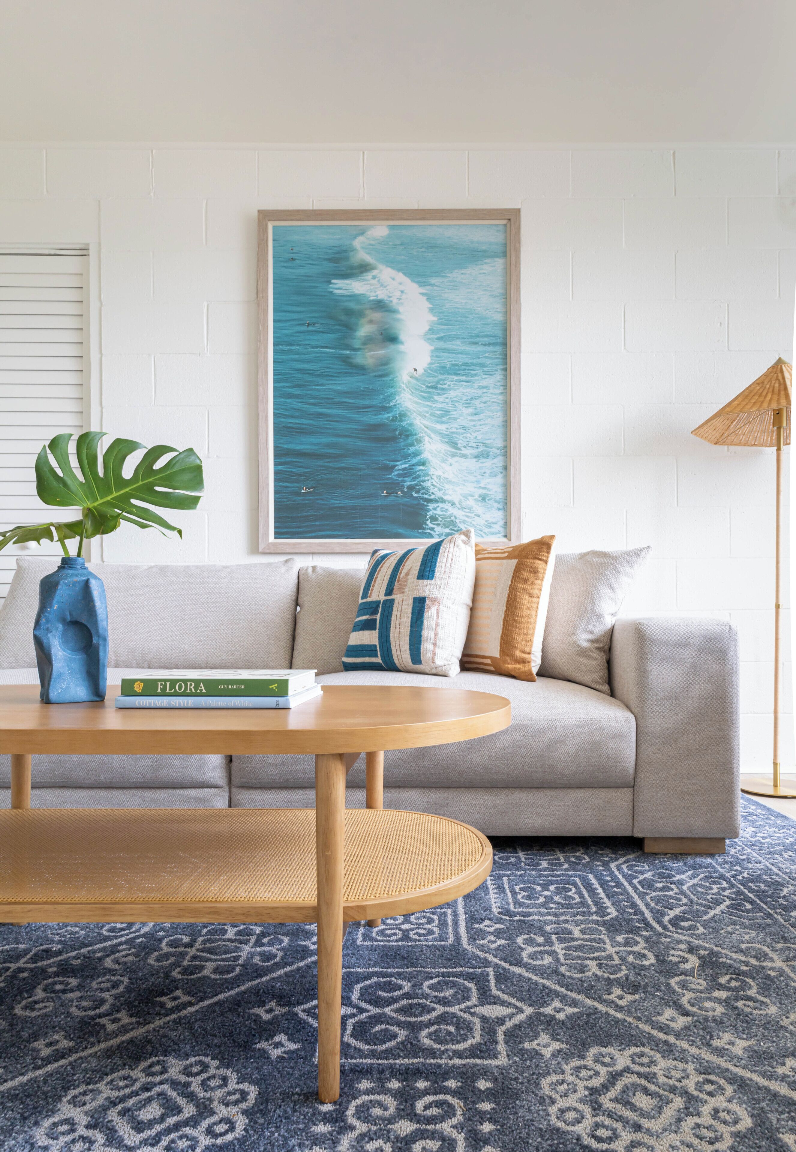 Sala de estar com sofá, mesa de centro, quadro da paisagem marítima, planta em vaso e luminária de chão.