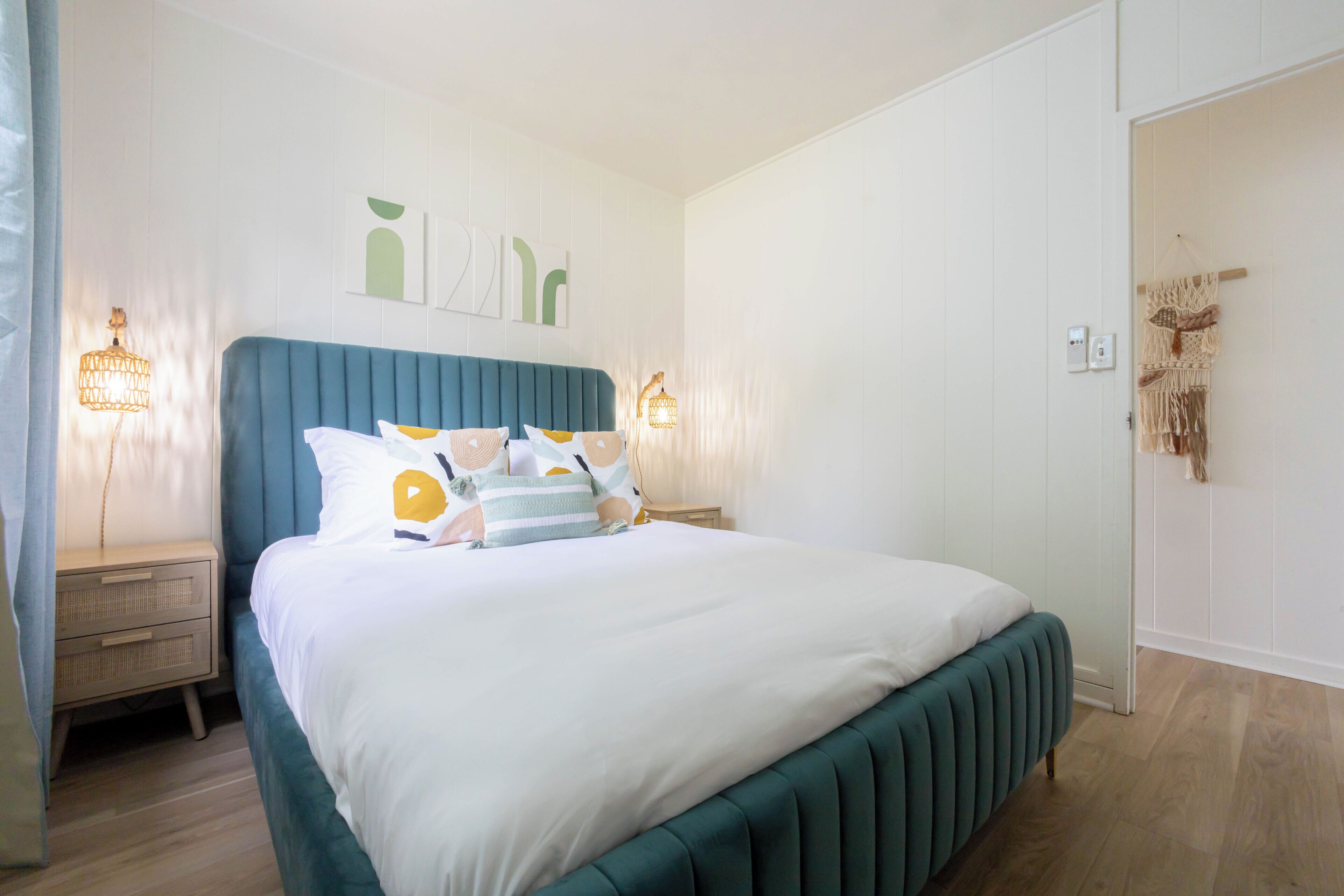 A bedroom with a bed, bedside tables, wall art, and a macrame wall hanging.