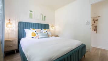 Quarto com cama, mesas de cabeceira, obra de arte na parede e um enfeite de macramé.