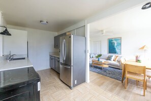 Uma cozinha moderna com geladeira embutida, uma sala de jantar com mesa e cadeiras de madeira, e uma sala de estar com sofá e um quadro na parede.