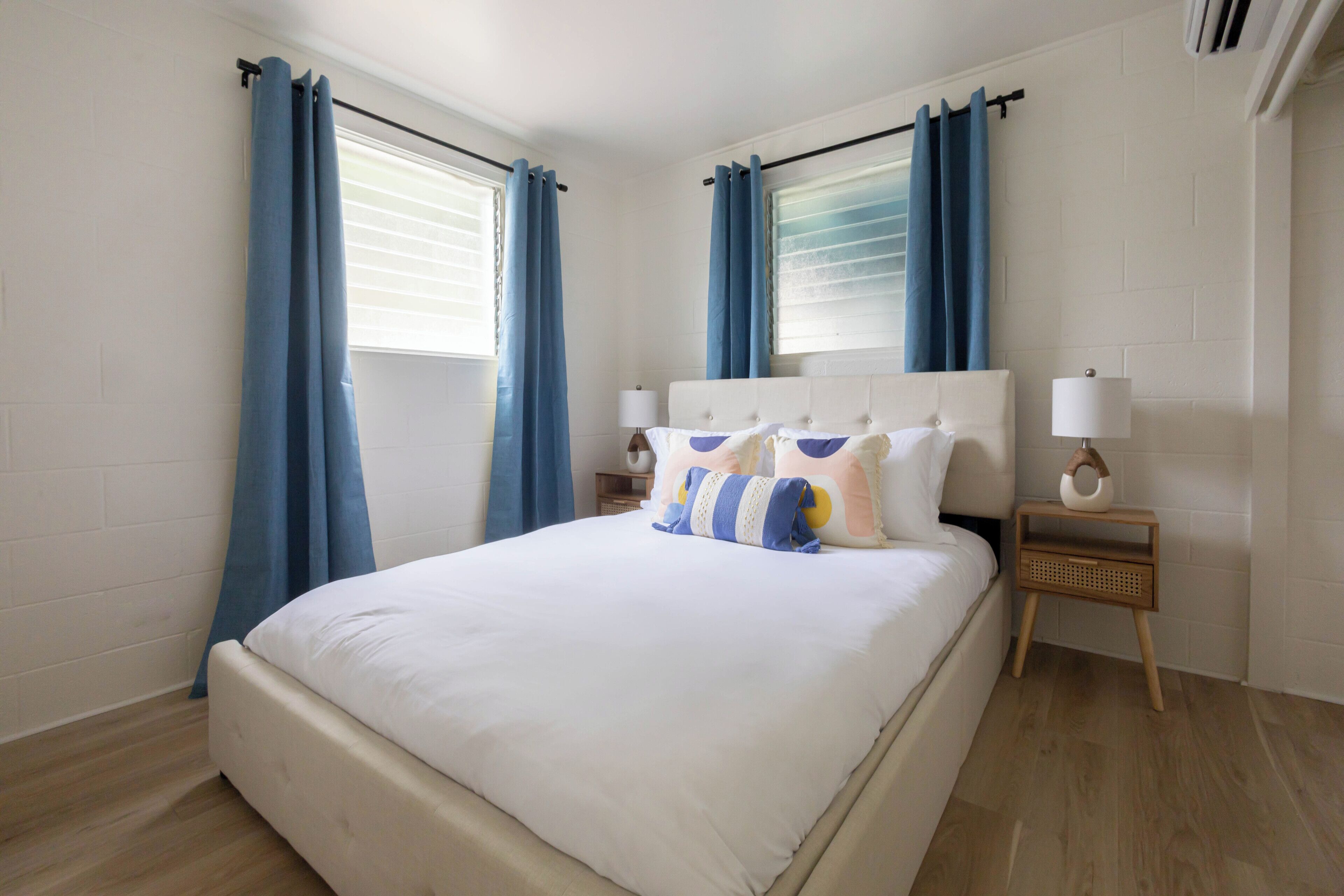 Quarto com cama grande, duas mesas de cabeceira, janela com cortinas e ar condicionado fixado na parede.