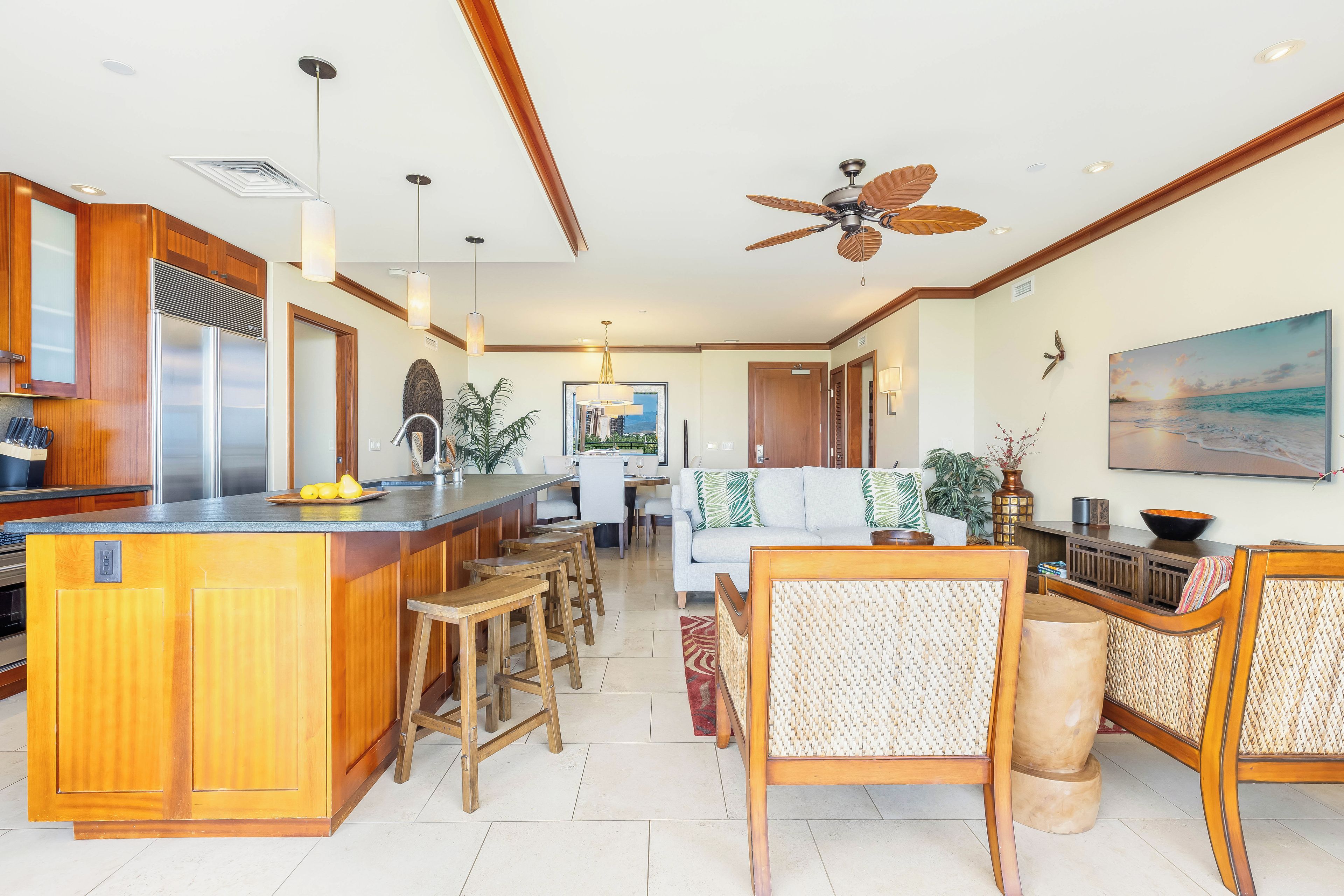 A spacious kitchen with a central island, wooden bar stools, a dining area with a white sofa, and a ceiling fan.