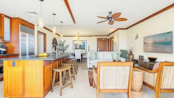 A spacious kitchen with a central island, wooden bar stools, a dining area with a white sofa, and a ceiling fan.