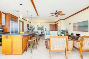 Une cuisine spacieuse dotée d’un îlot central, de tabourets de bar en bois, d’un coin repas avec un canapé blanc et d’un ventilateur de plafond.