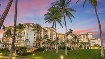 A multi-story hotel with balconies, palm trees, and a well-lit pathway.