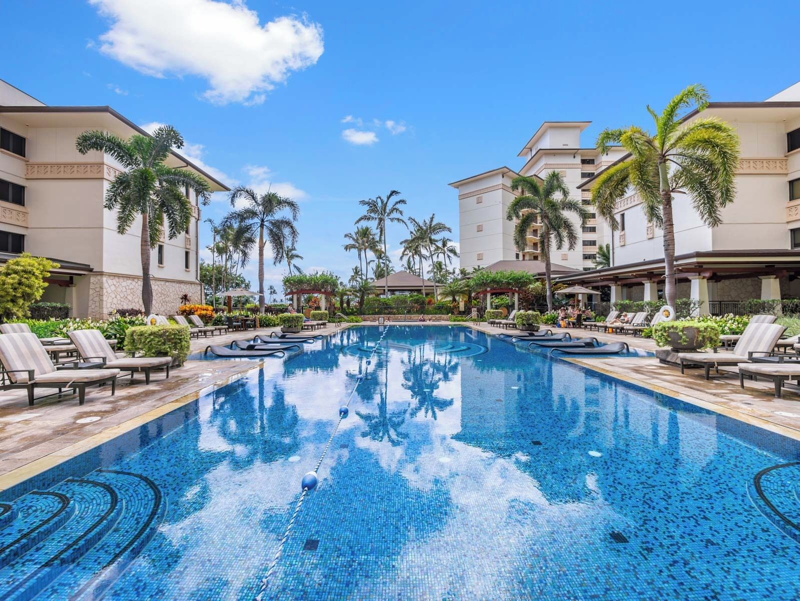 A swimming pool with lounge chairs and palm trees, surrounded by buildings with a modern design.
