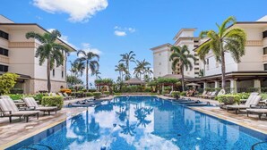 A swimming pool with lounge chairs and palm trees, surrounded by buildings with a modern design.