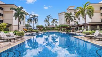 A swimming pool with lounge chairs and palm trees, surrounded by buildings with a modern design.