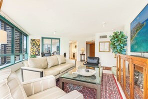 Ein modernes Wohnzimmer mit einem beigen Sofa, einem Glastisch und einem roten Teppich mit Muster.