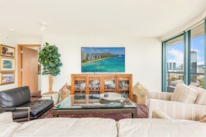 Ein Wohnzimmer mit Glastisch, einer Couch, einer Vitrine und einem großen Fenster mit Blick auf die Stadt.