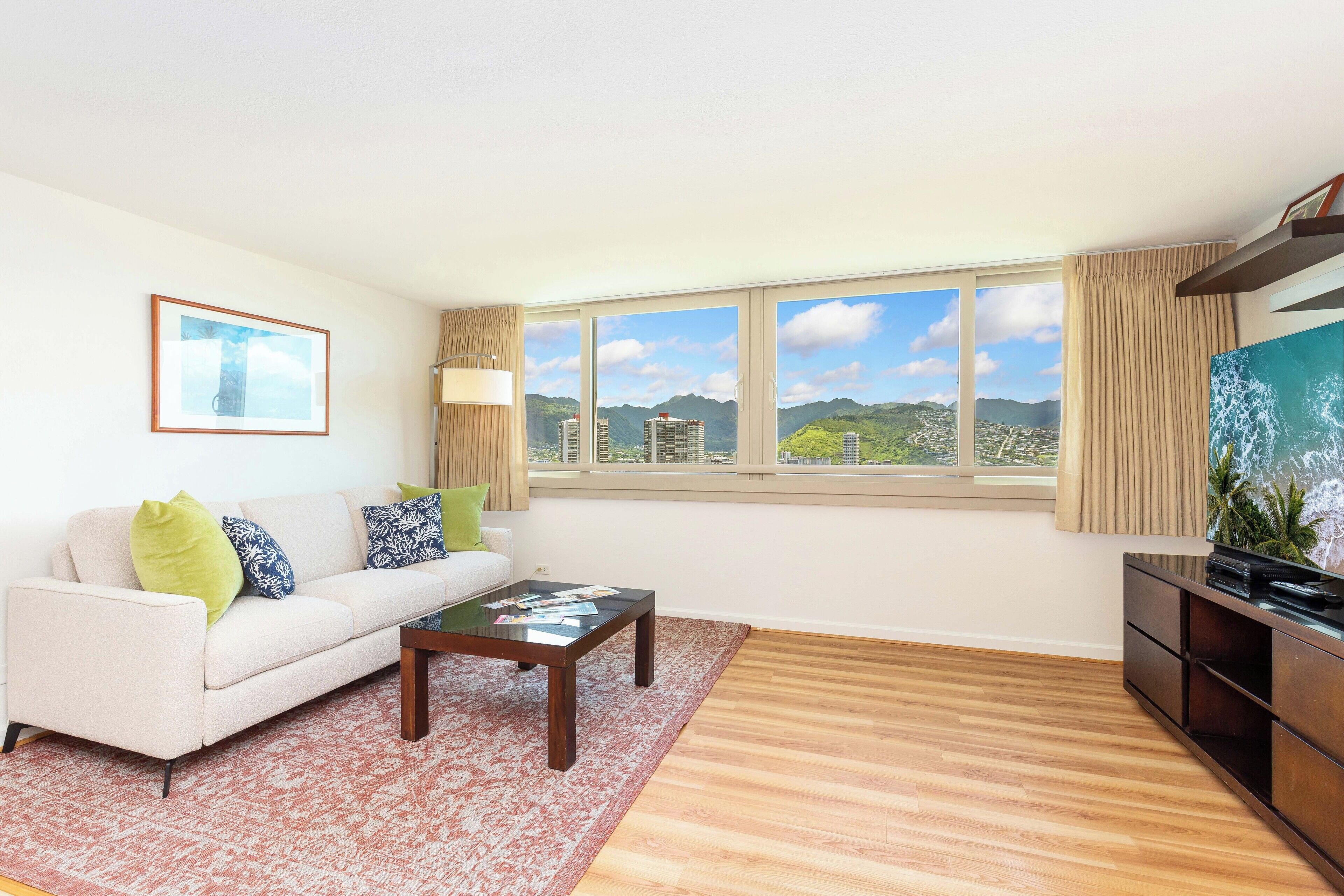 A living room with a white sofa, a glass coffee table, and a large window with a city view.