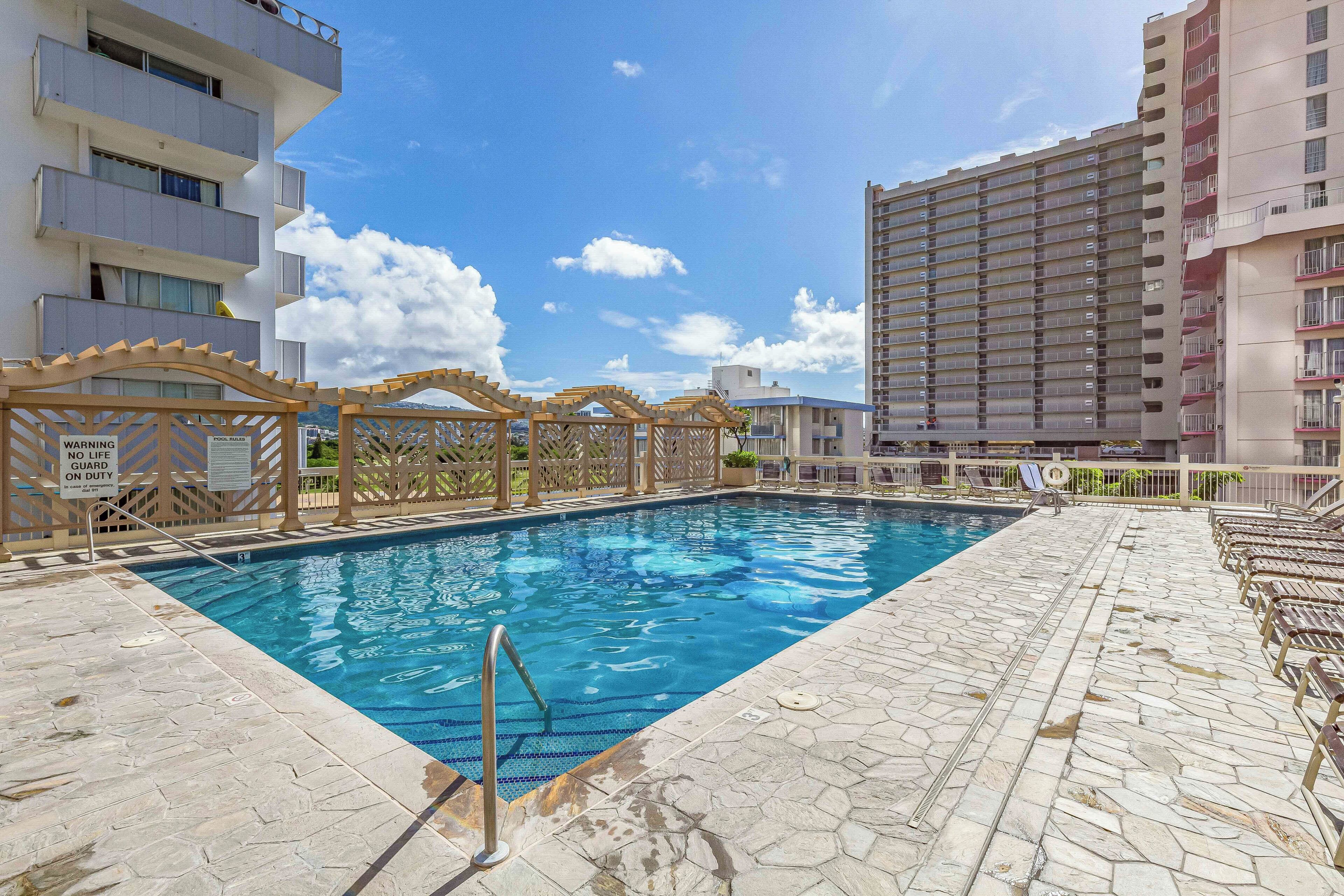 A swimming pool with a wooden deck and a safety sign, surrounded by buildings.