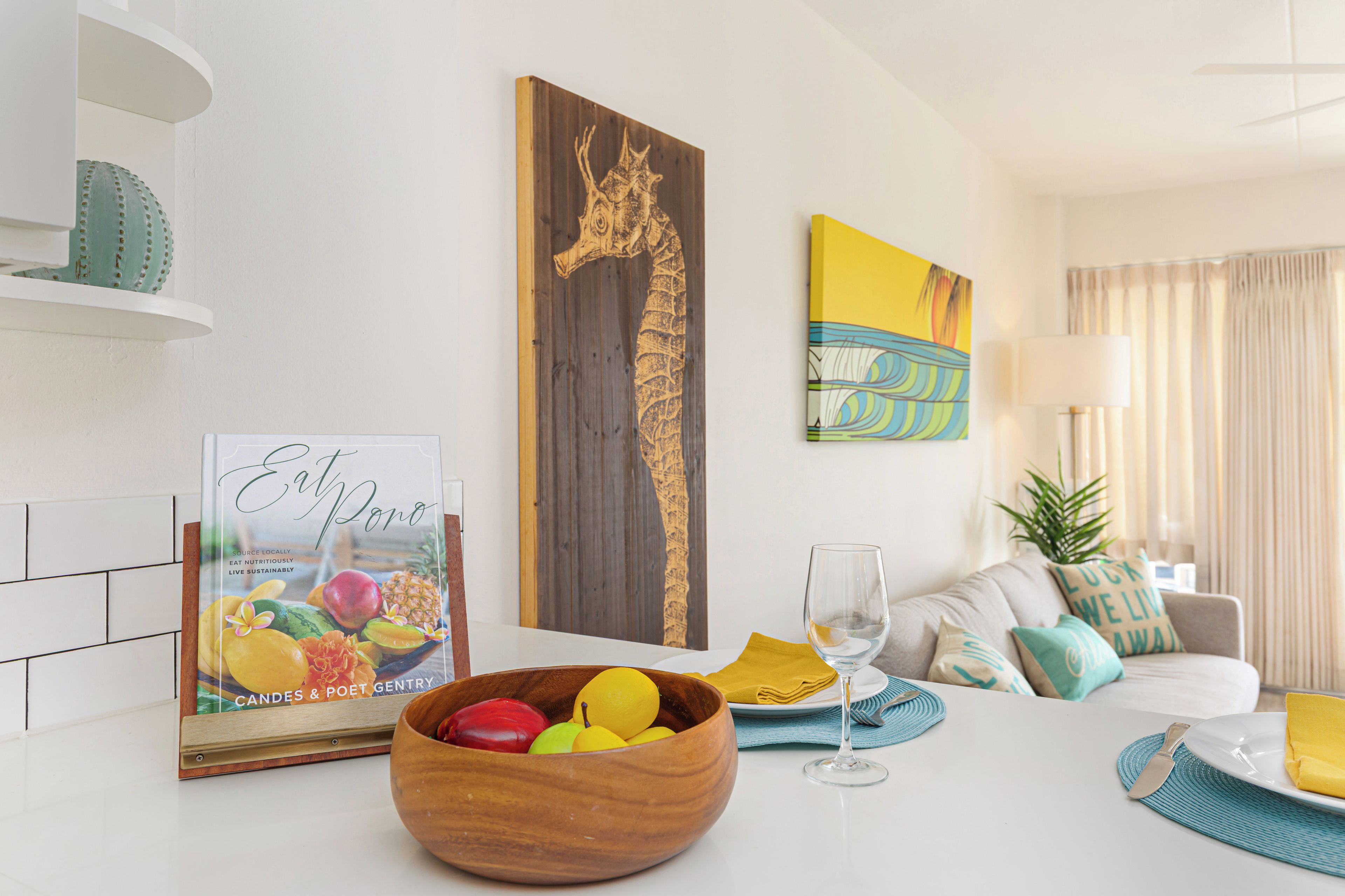 Un salon moderne avec une table à manger en bois, un panier de fruits, un tableau encadré et un canapé avec des coussins.